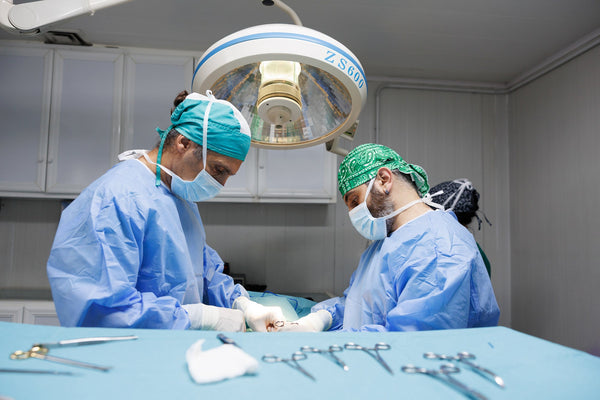 Two surgeons in an operating room with surgical tools on a table.